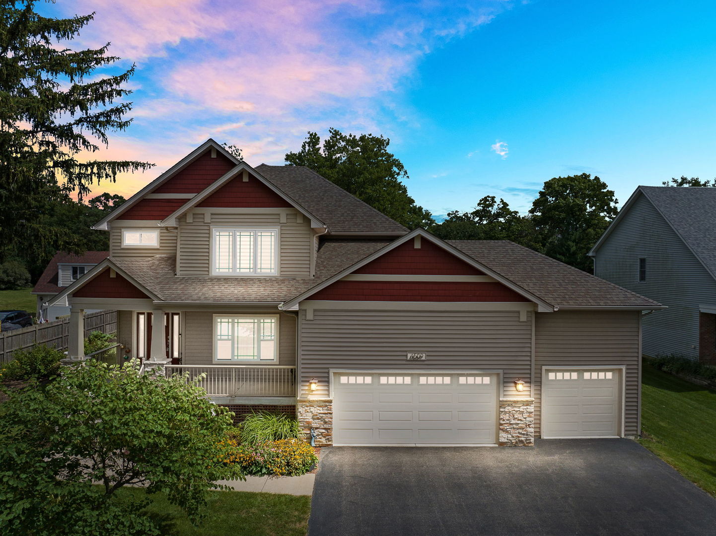 Two-story gray house with red gables, stone accents, a covered porch, and two garages at dusk.