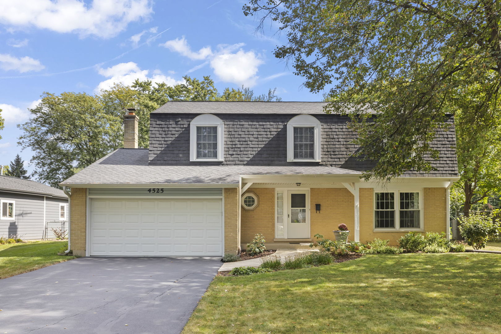 Yellow-brick house with two dormer windows, a double garage, and a covered front entry.