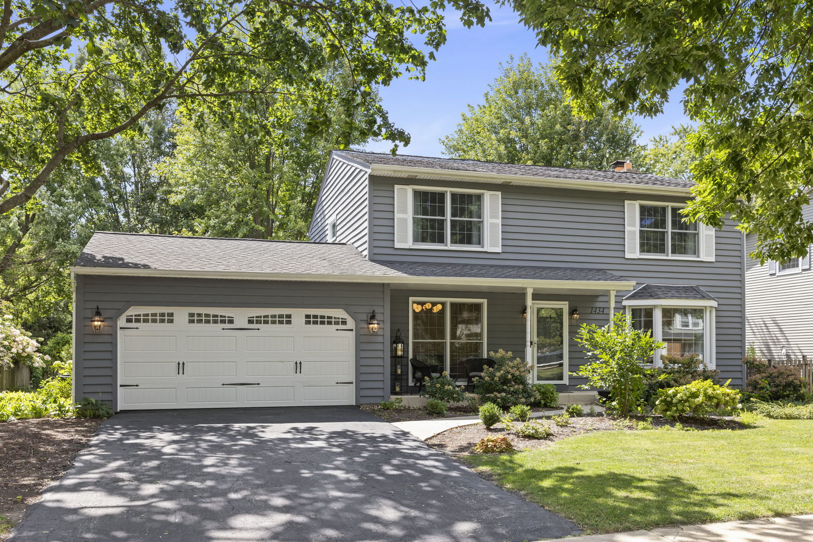 Gray two-story house with a white double garage and leafy trees framing the front yard.