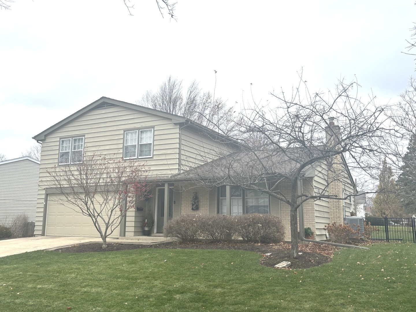 Two-story house with an attached garage, leafless front-yard trees, and a fenced side yard.