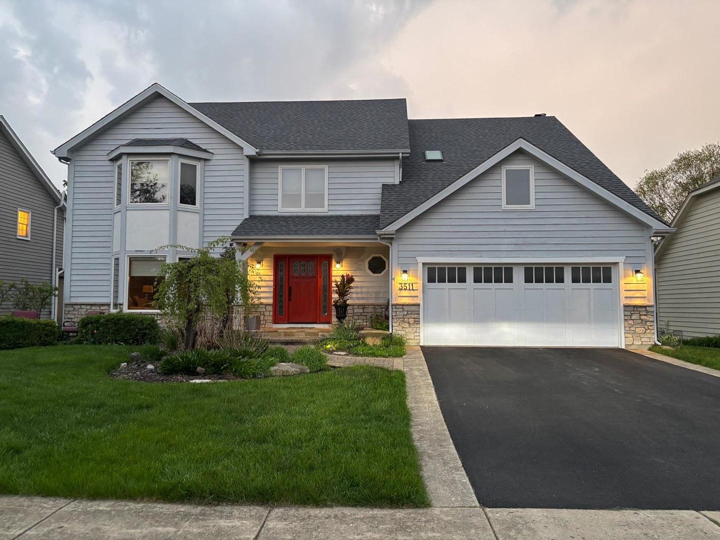 Two-story gray house with a red front door, stone accents, and a double garage at dusk.