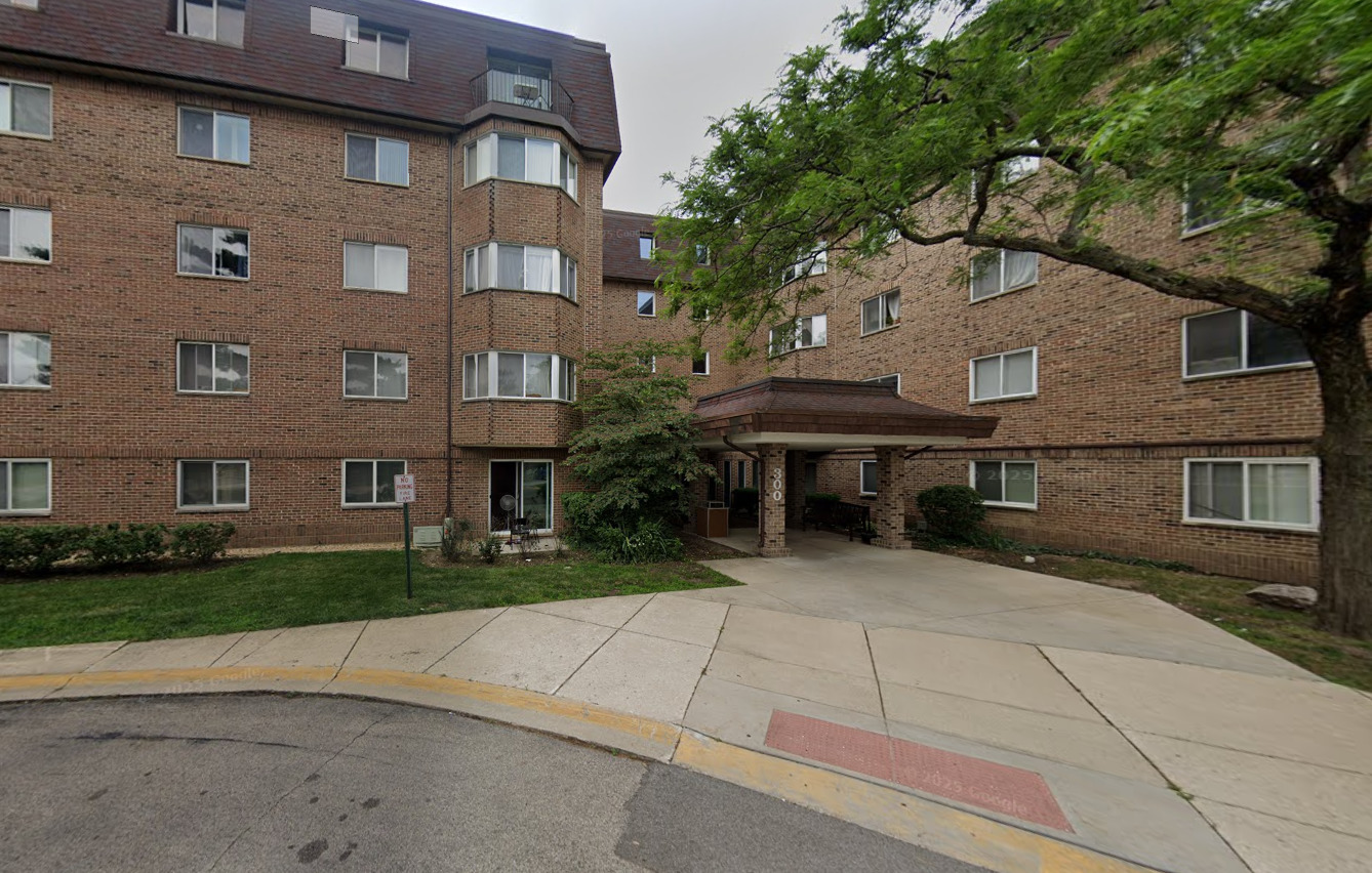 Brick apartment building with a covered entrance marked 300 and a large tree beside the sidewalk.