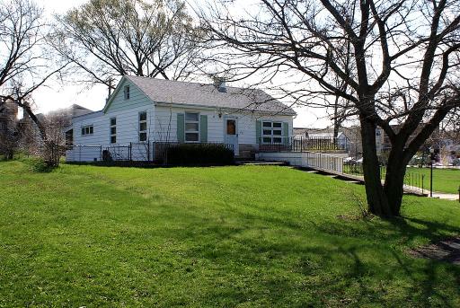 Light blue single-story house behind a broad lawn, framed by large leafless trees.