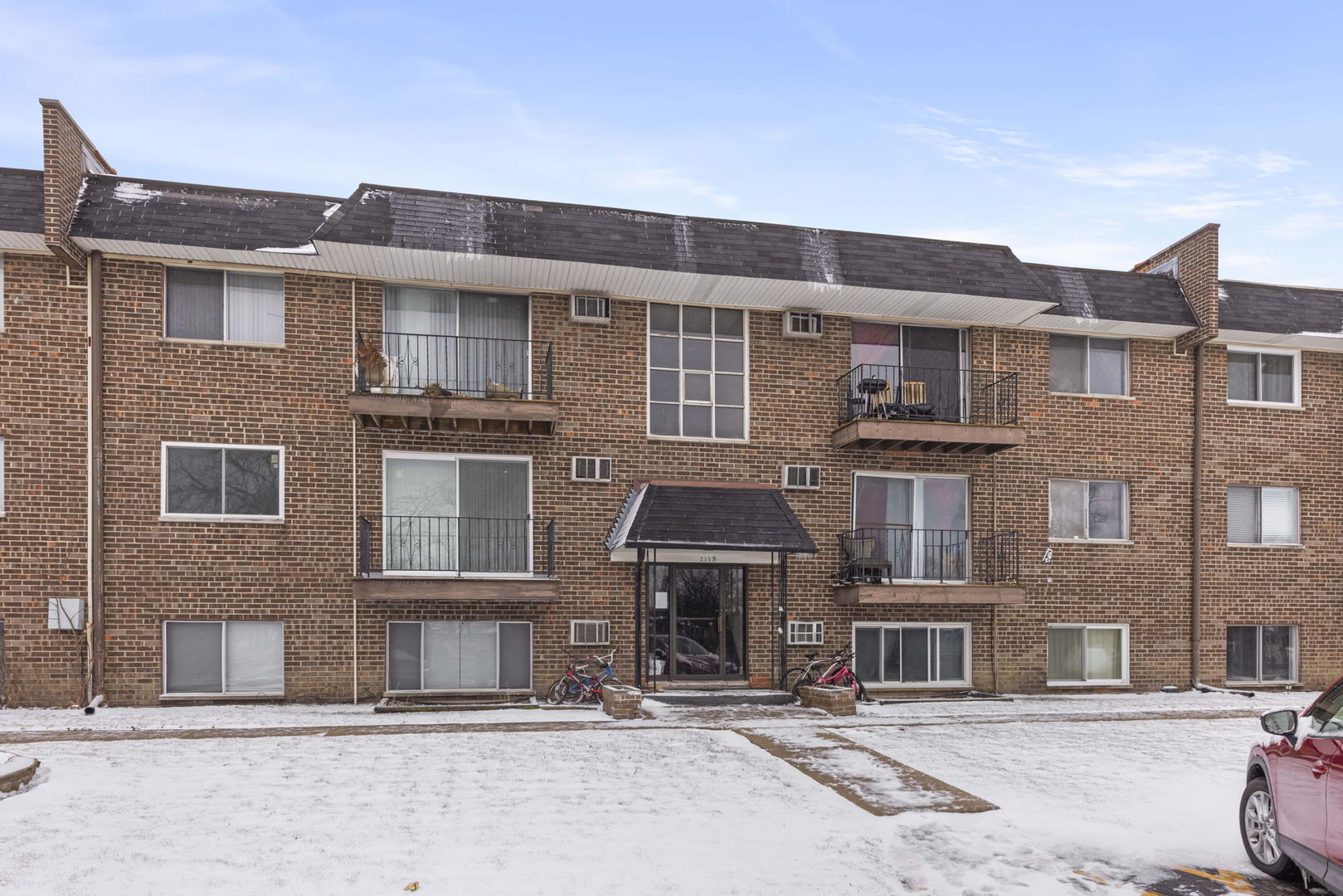 Three-story brick apartment building with balconies and a snow-covered lawn.