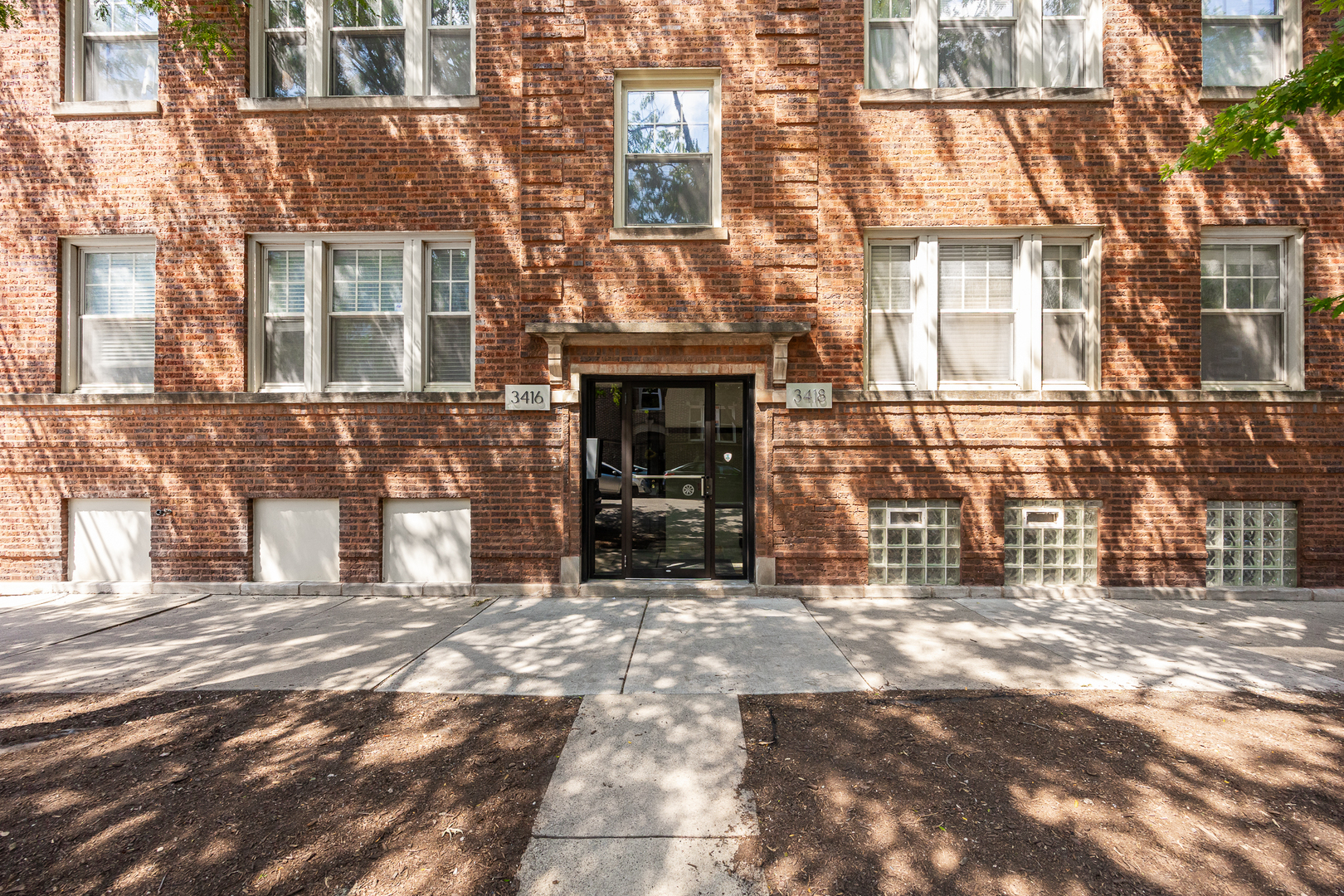 Red brick apartment building with a central glass entrance and address plaques reading 3416 and 3418.
