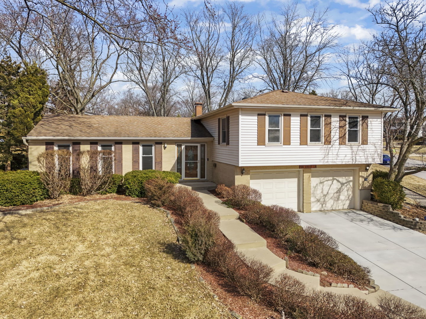 Split-level home with white siding, tan brick, two garage doors, and a curved front walkway.