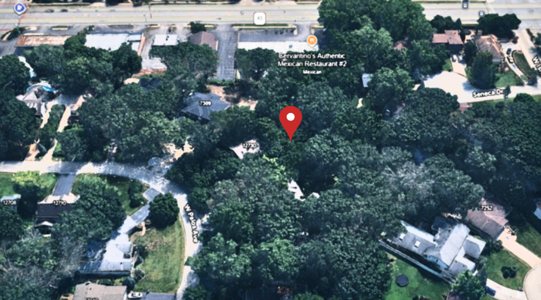 Aerial view of a tree-covered residential property marked by a red pin, surrounded by homes and streets.