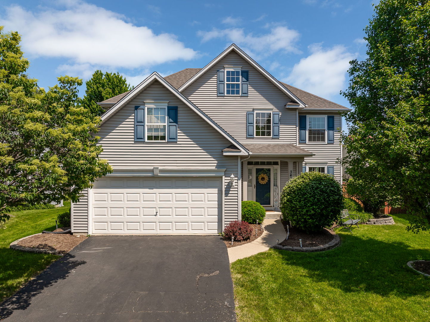 Two-story gray house with blue shutters, a double garage, and landscaped front lawn.