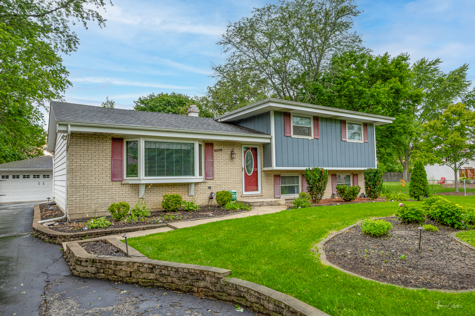Split-level home with tan brick, blue-gray siding, red front door, and landscaped front lawn.