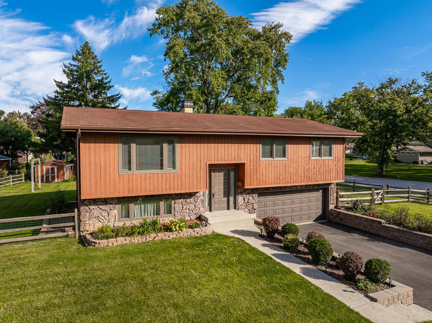Split-level home with reddish-brown siding, stone lower level, attached garage, and landscaped front yard.