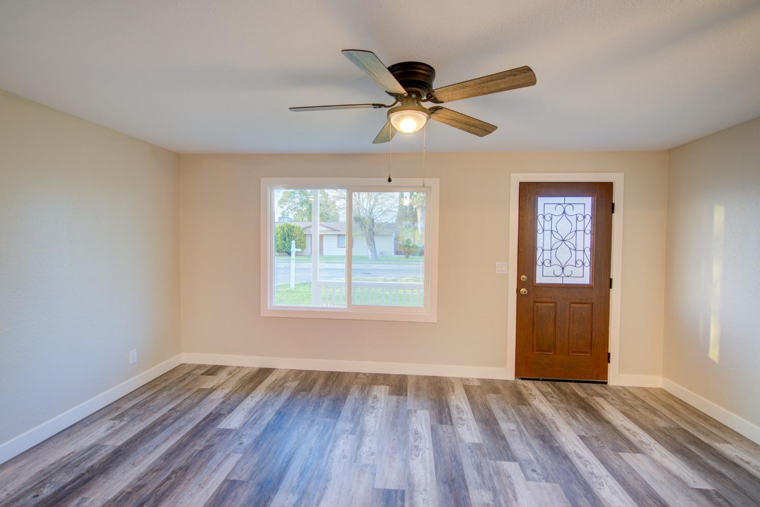 Empty room with a decorative-glass front door, large window, ceiling fan, and gray plank flooring.