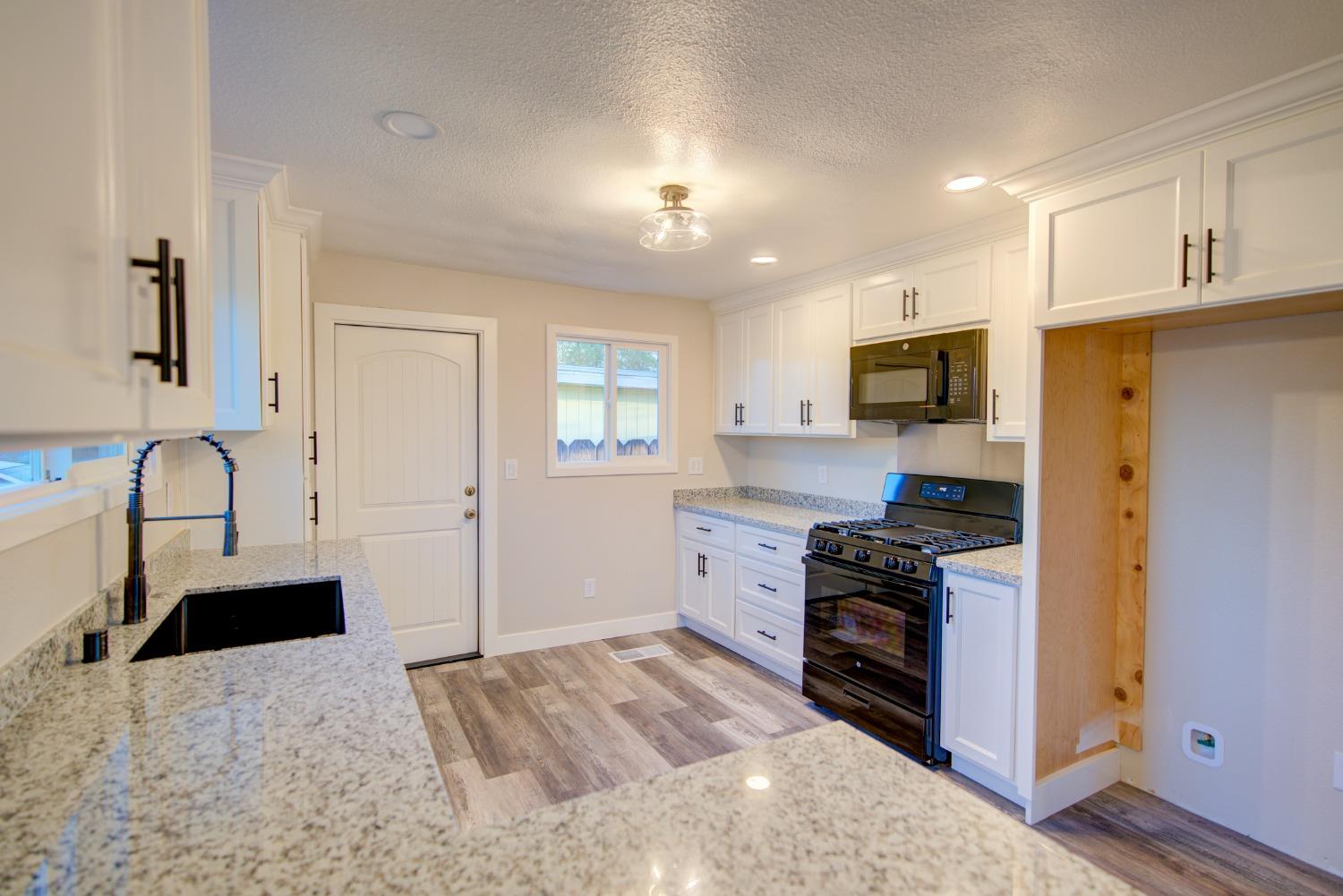 Bright kitchen with white cabinets, granite counters, black appliances, and wood-look flooring.