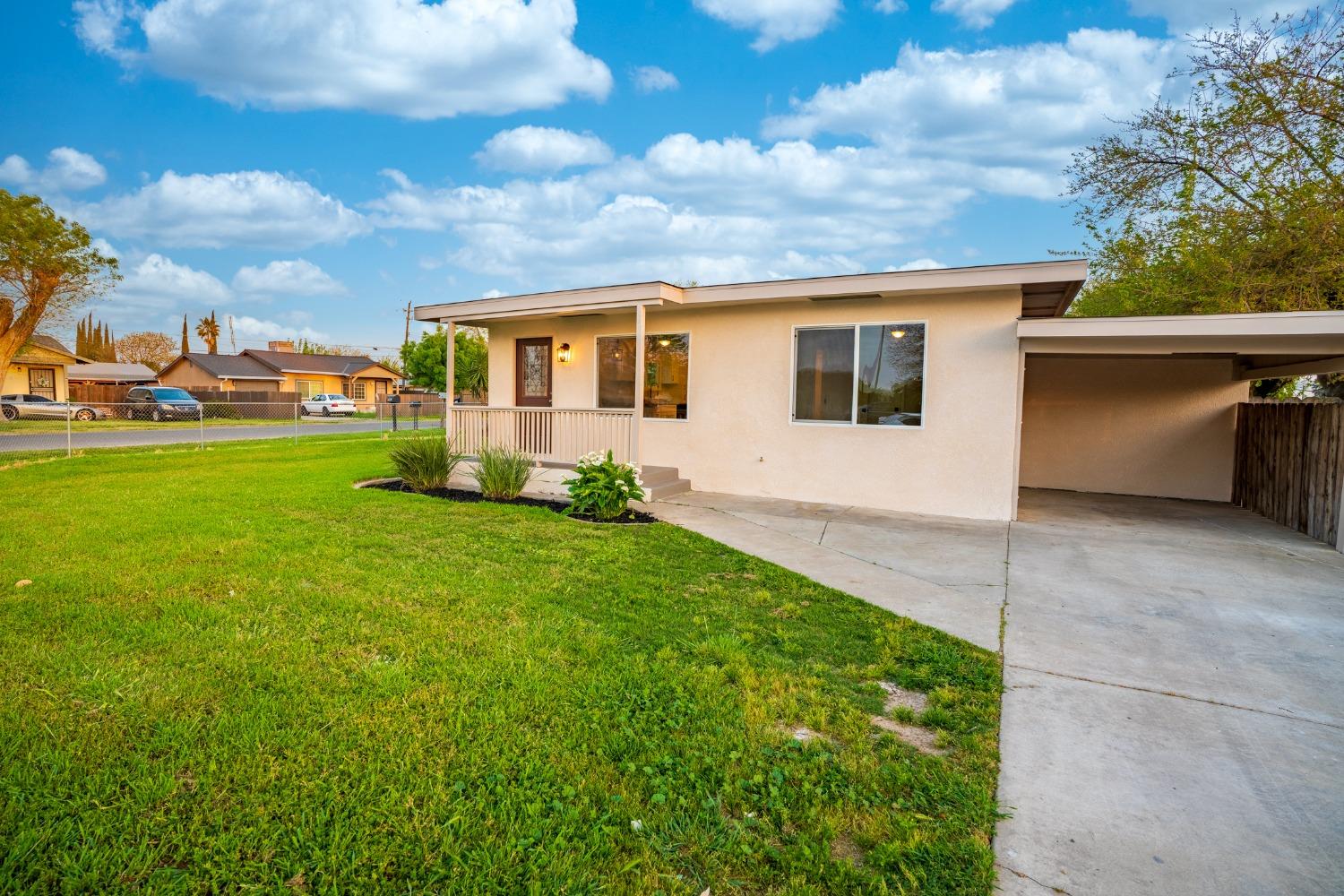 Single-story house with a covered porch, attached carport, green lawn, and concrete driveway.