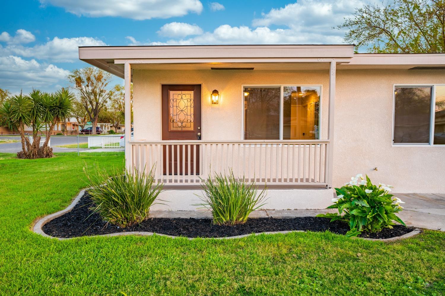 Beige stucco home with a covered porch, decorative entry door, and landscaped front lawn.