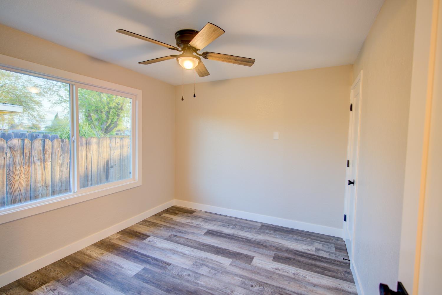 Empty bedroom with gray plank flooring, a ceiling fan, and a large window.