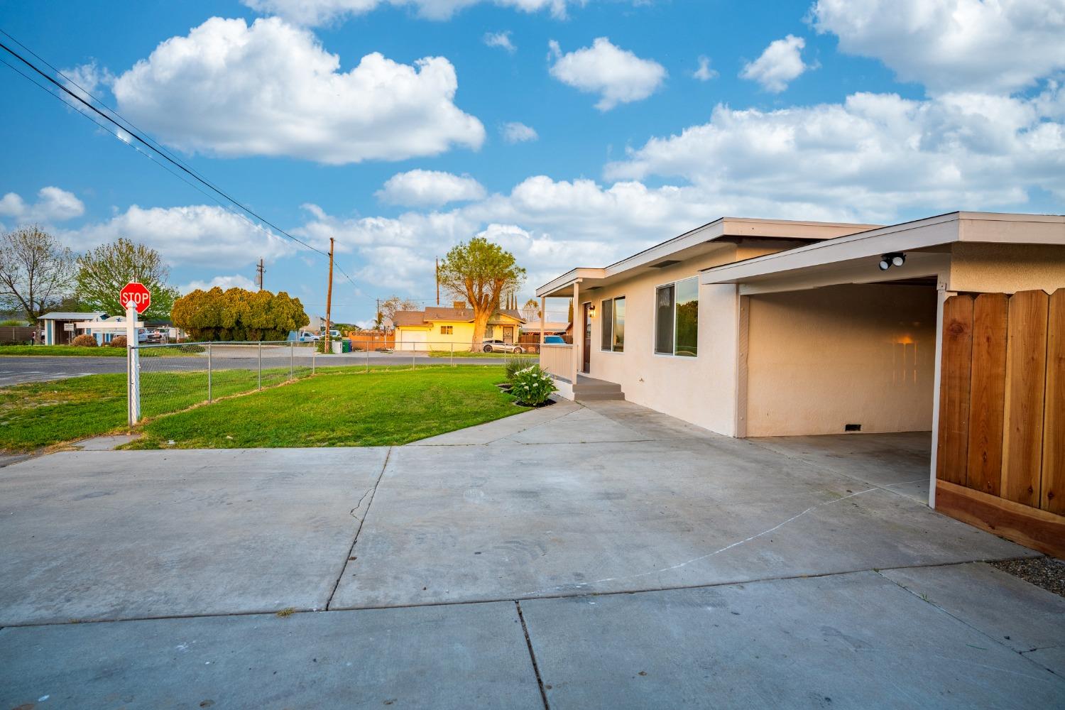Single-story house with a covered carport, broad concrete driveway, and fenced lawn.