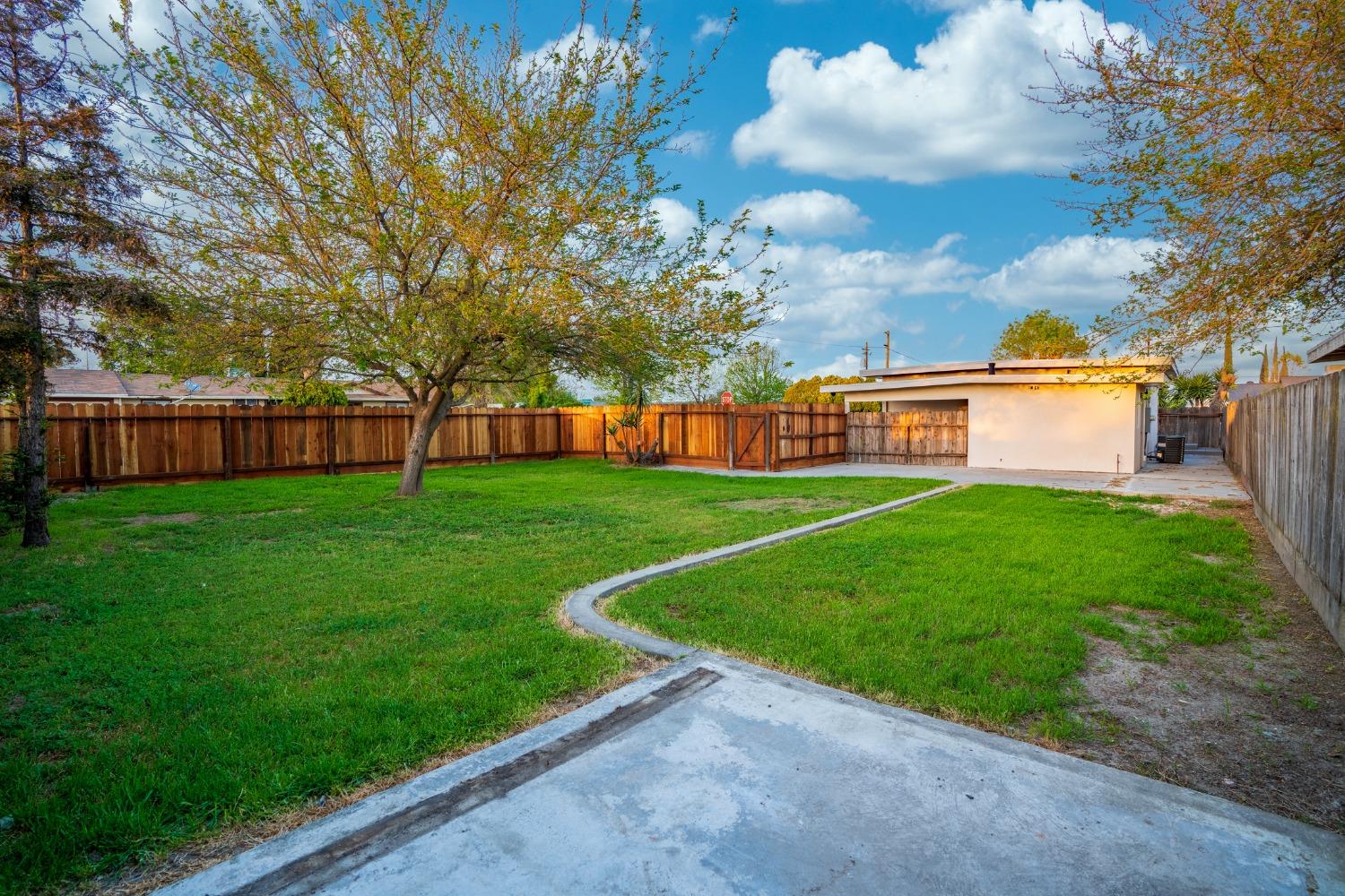 Fenced backyard with a broad lawn, mature tree, and small outbuilding at the rear.