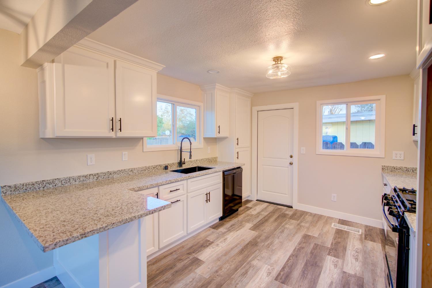 Unfurnished kitchen with white cabinets, granite counters, a black sink, and wood-look flooring.