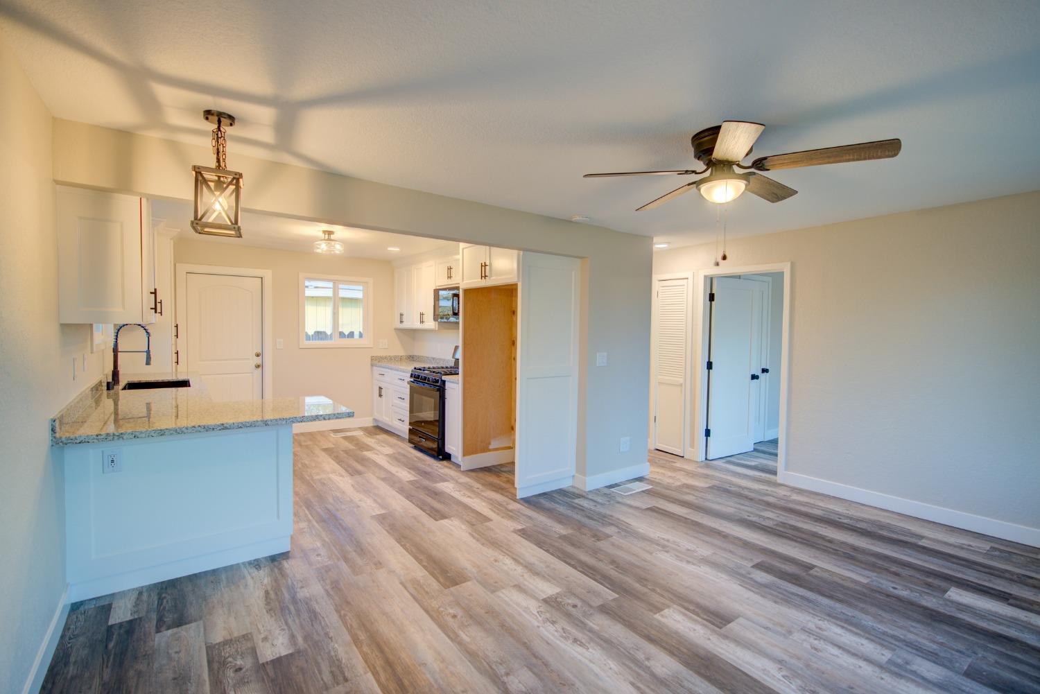 Open-plan kitchen and living area with a granite peninsula, white cabinets, and wood-look floors.