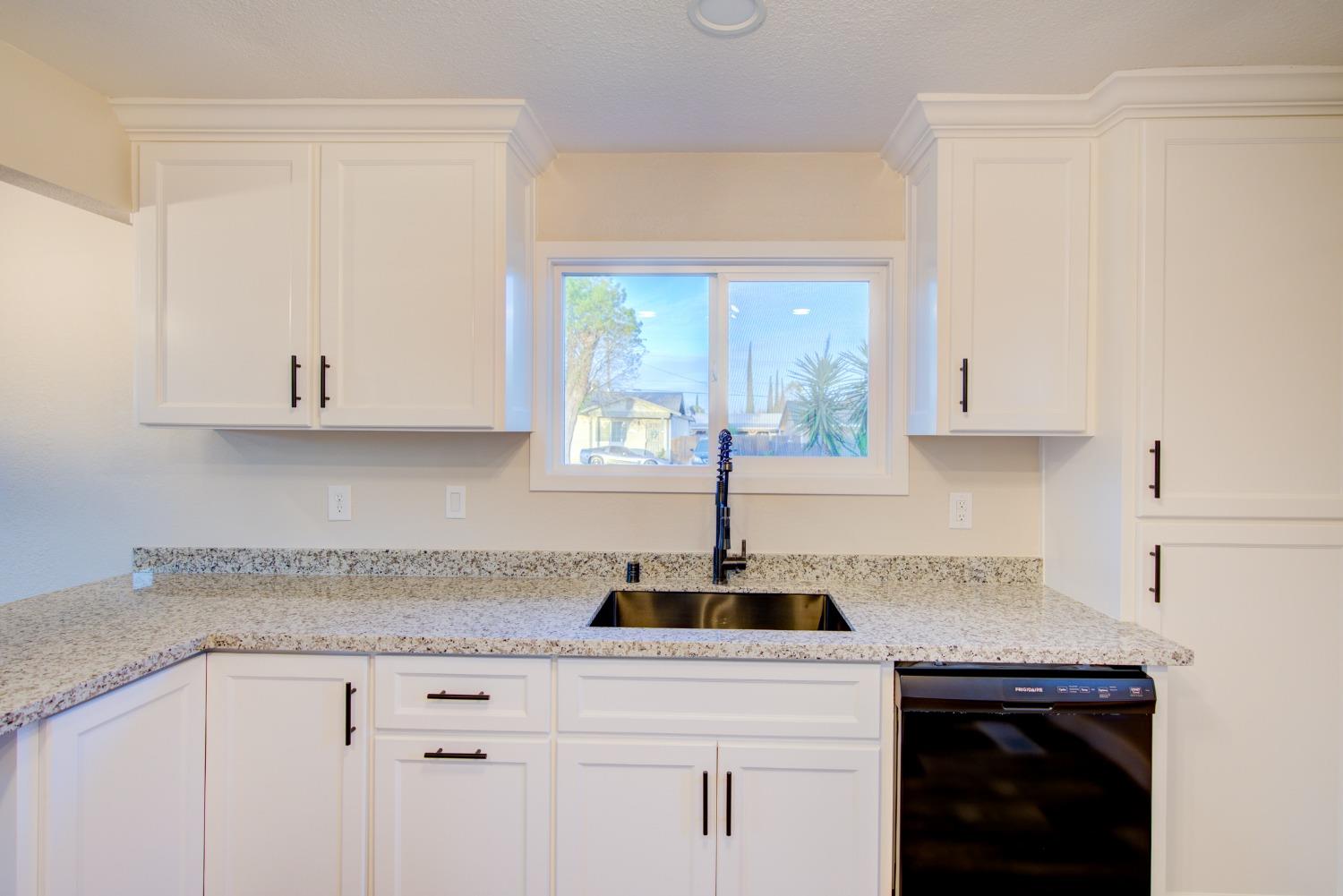 Kitchen with white shaker cabinets, speckled stone counters, a black sink, and a window.