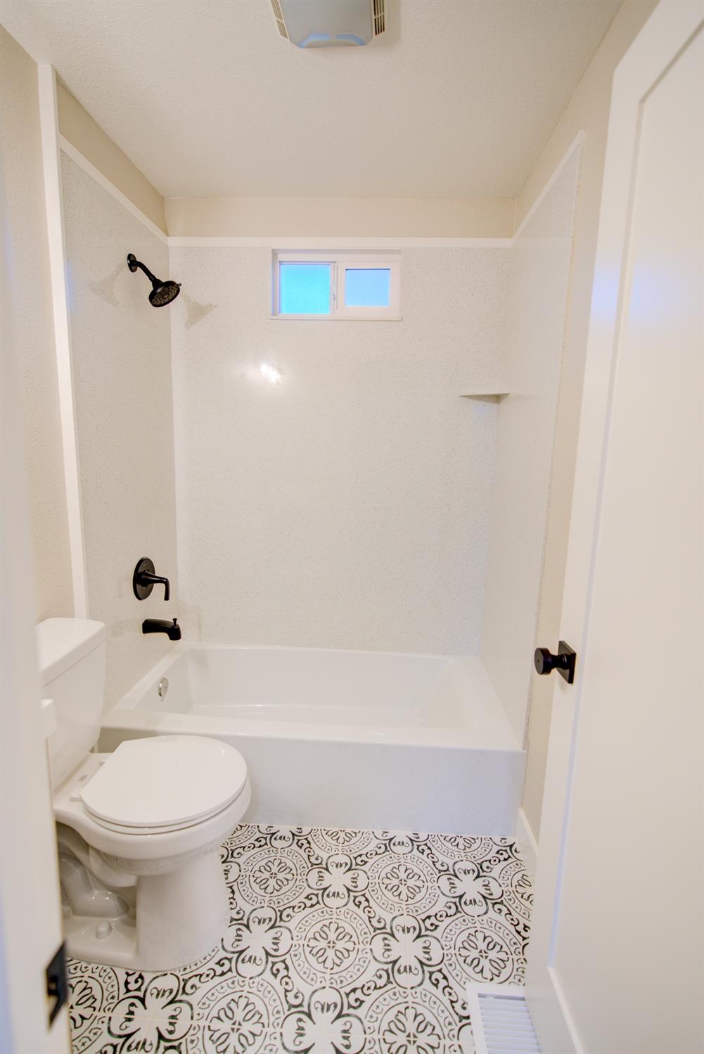 Bathroom with a white tub, black shower fixtures, and patterned floor tile.