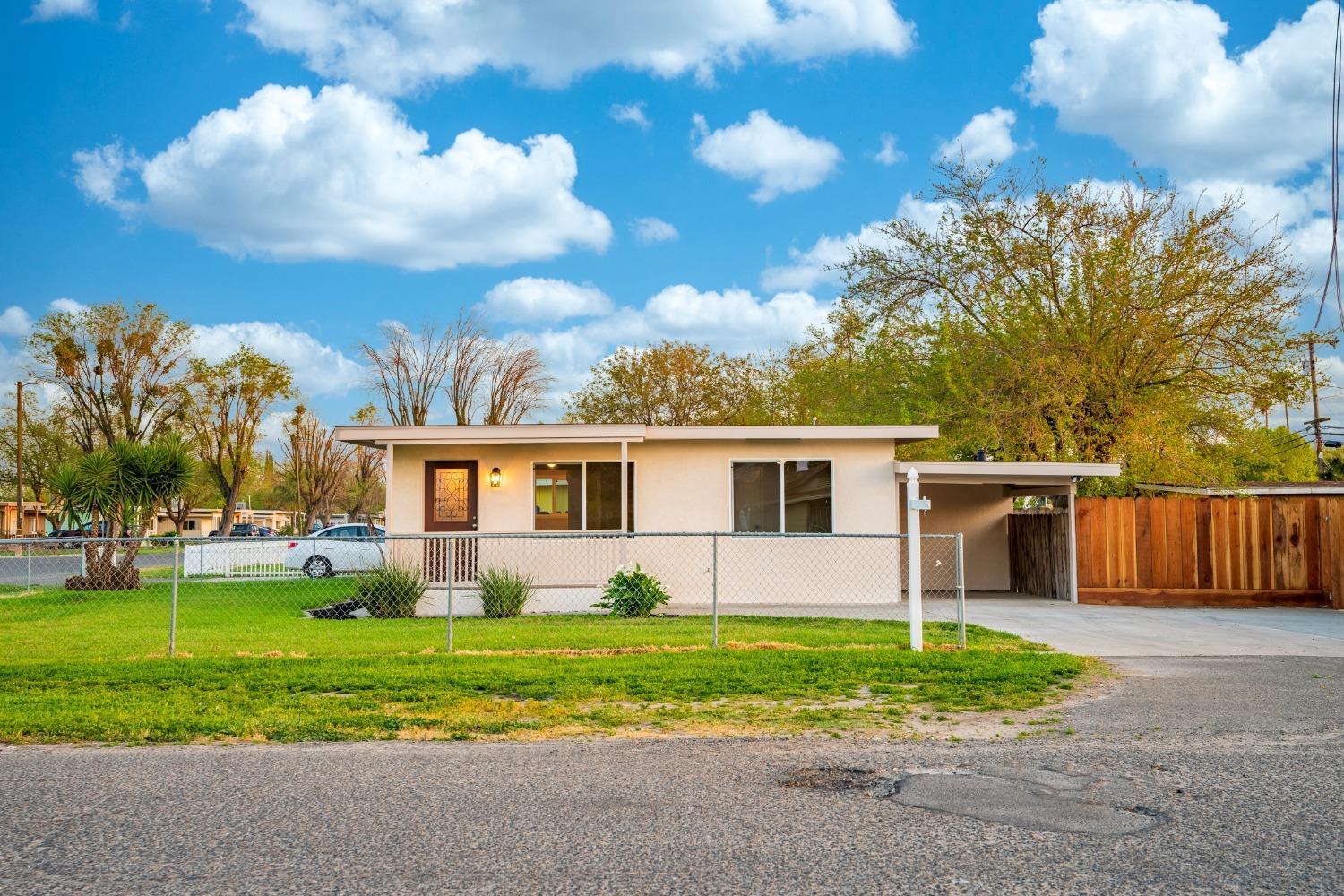 Single-story home with a flat roof, chain-link fence, green lawn, and covered carport.