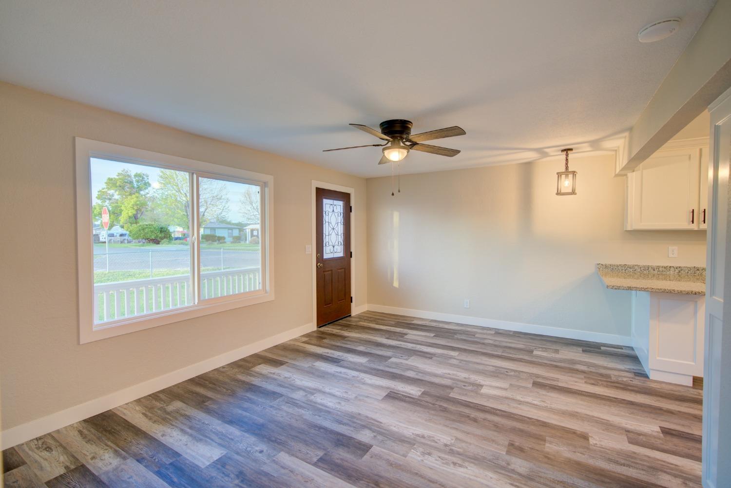Empty living area with gray plank flooring, ceiling fan, and large front window.