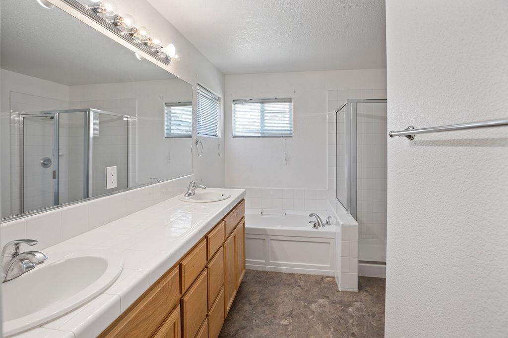 Bathroom with a long double vanity, wood cabinets, bathtub, and two glass-enclosed showers.