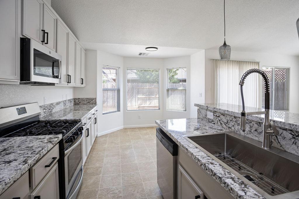 Bright kitchen with granite counters, white cabinetry, stainless appliances, and a large island sink.