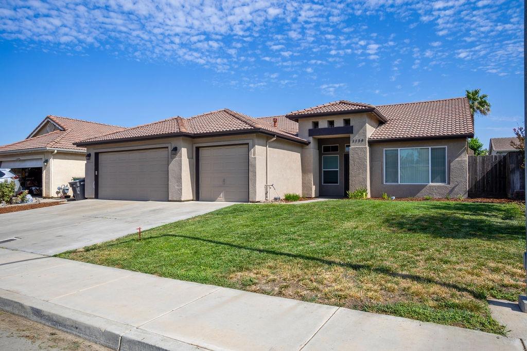 Single-story stucco home with a tiled roof, two-car garage, wide driveway, and front lawn.