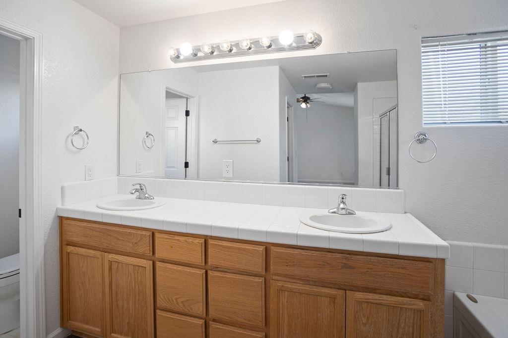Bathroom with a double-sink wood vanity, tiled countertop, and large mirror.