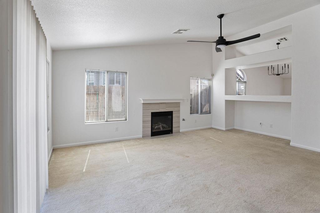 Vacant living room with a gas fireplace, black ceiling fan, and large windows.