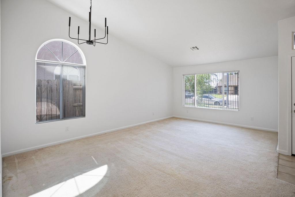 Empty living room with beige carpet, an arched window, and a black chandelier.