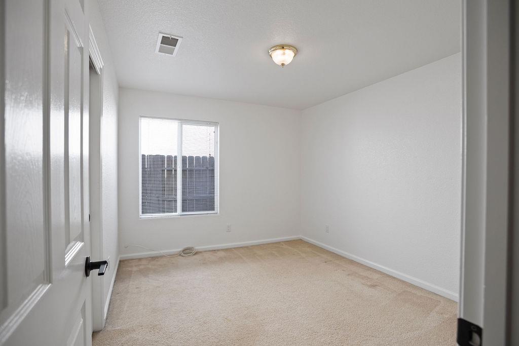 Empty bedroom with beige carpet, white walls, and a window with blinds.