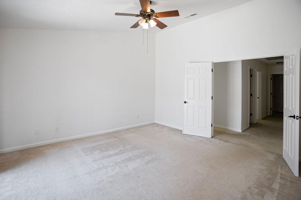 Empty carpeted bedroom with a wooden ceiling fan and open doors to a hallway.