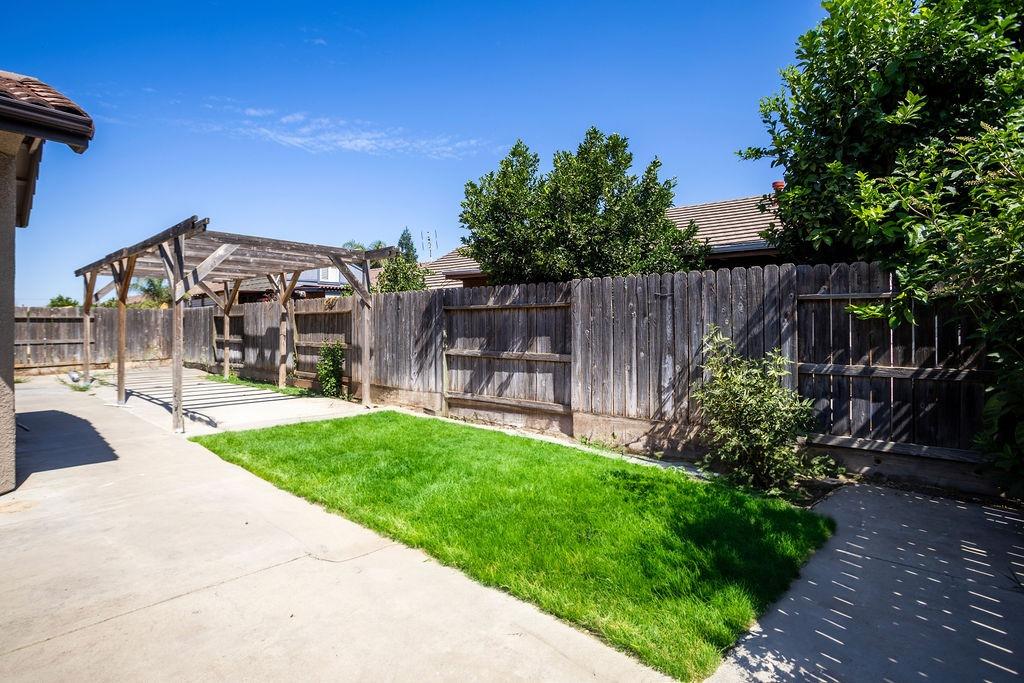 Backyard patio with a wooden pergola, bright green lawn, and tall wooden fencing.