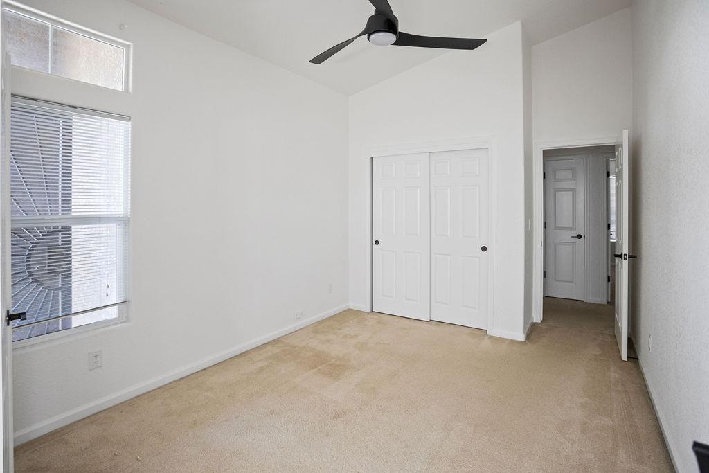 Empty bedroom with beige carpet, sliding closet doors, and a black ceiling fan.