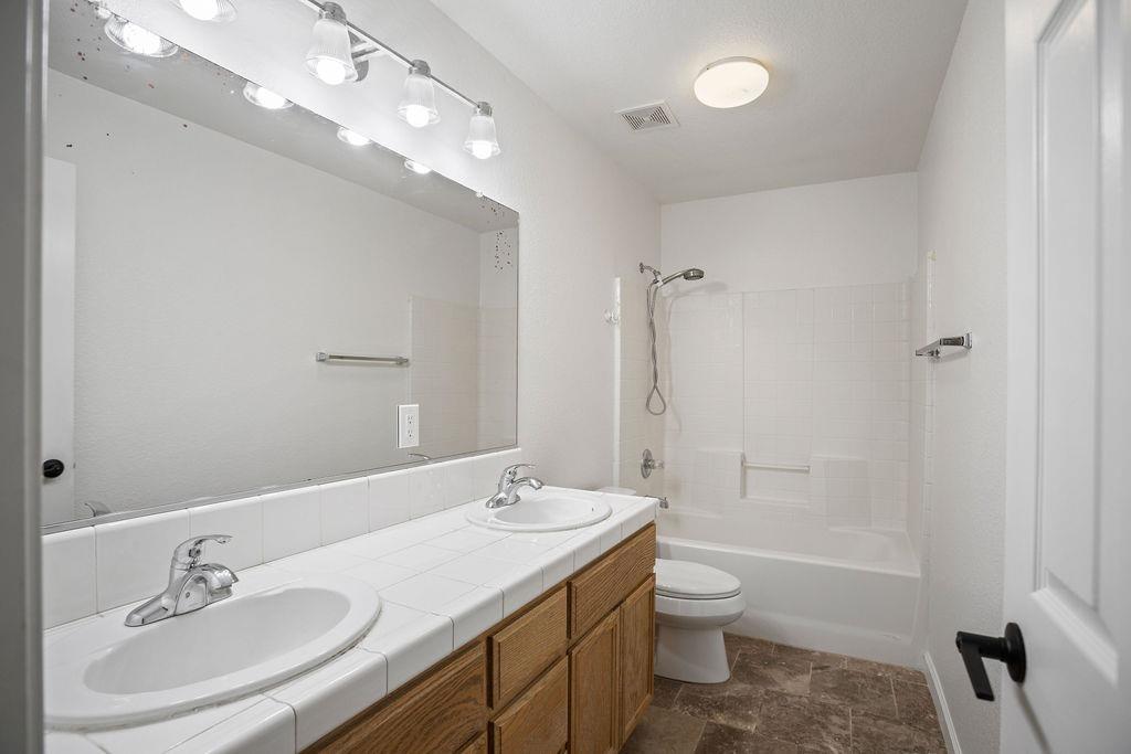 Bathroom with a tiled double-sink vanity, wood cabinets, and a white tub-shower.