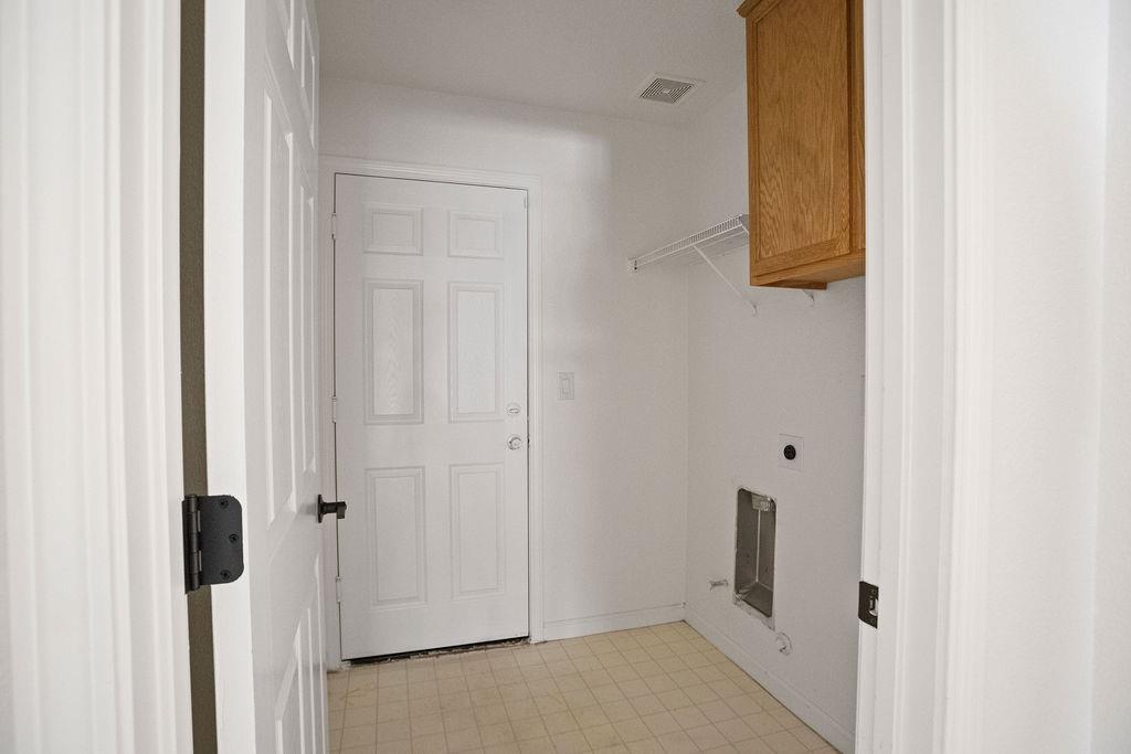 Empty laundry room with washer hookups, wire shelf, and upper wood cabinet.