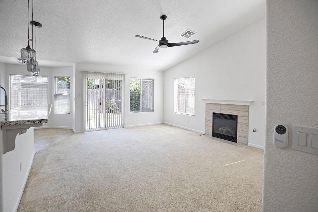 Empty living room with a tiled fireplace, ceiling fan, and sliding glass doors to a fenced yard.