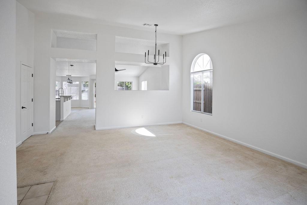 Empty living room with beige carpet, a black chandelier, and an arched window.
