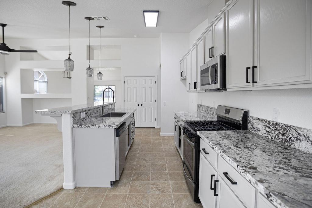 Kitchen with a large stone island, white cabinets, and stainless steel appliances.