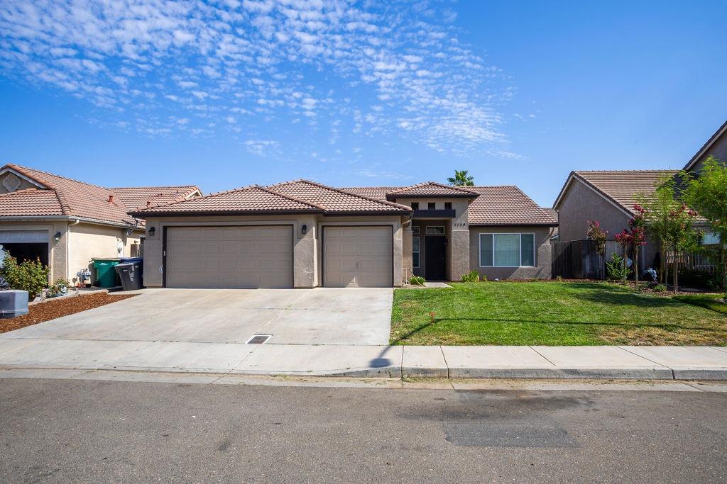 Single-story stucco home with a tile roof, two-car garage, wide driveway, and front lawn.