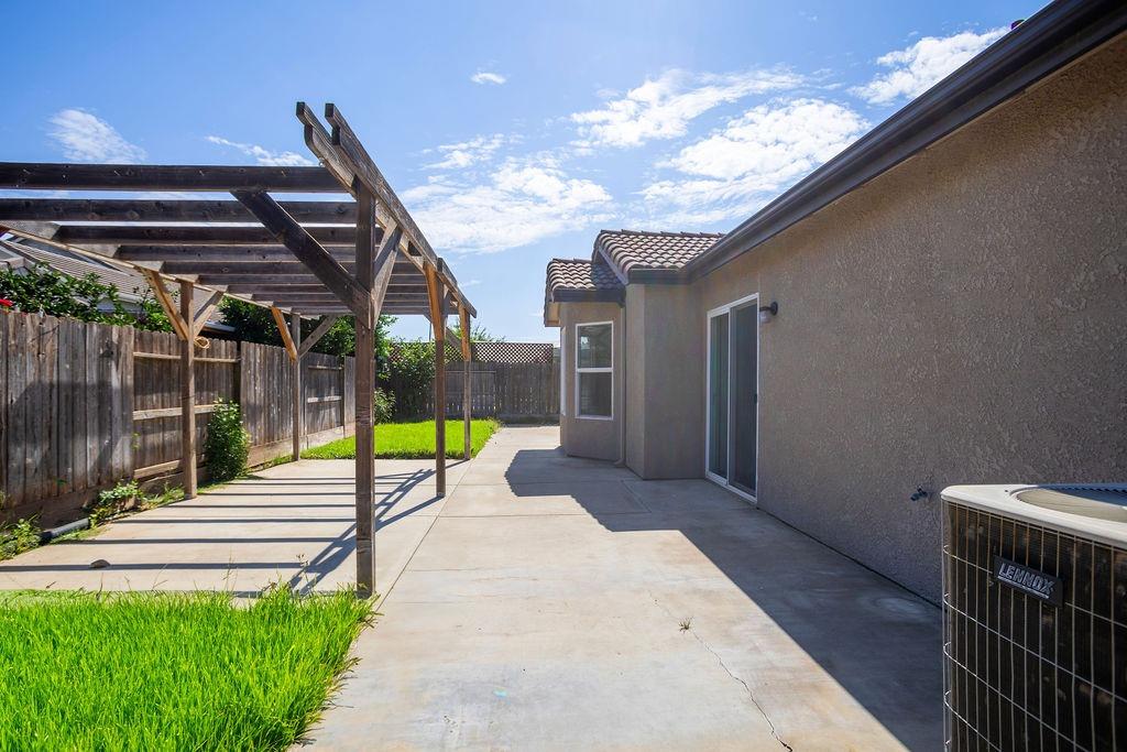Backyard patio with a wooden pergola, concrete paving, and a strip of lawn beside the house.