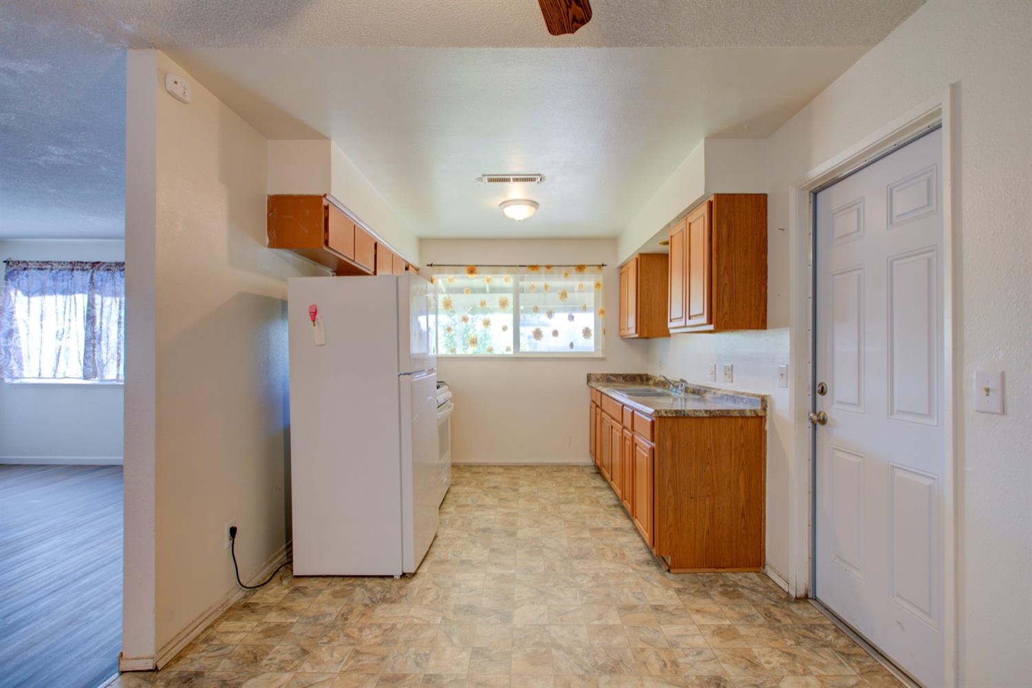 Kitchen with wood cabinets, white appliances, and a sink beneath a curtained window.