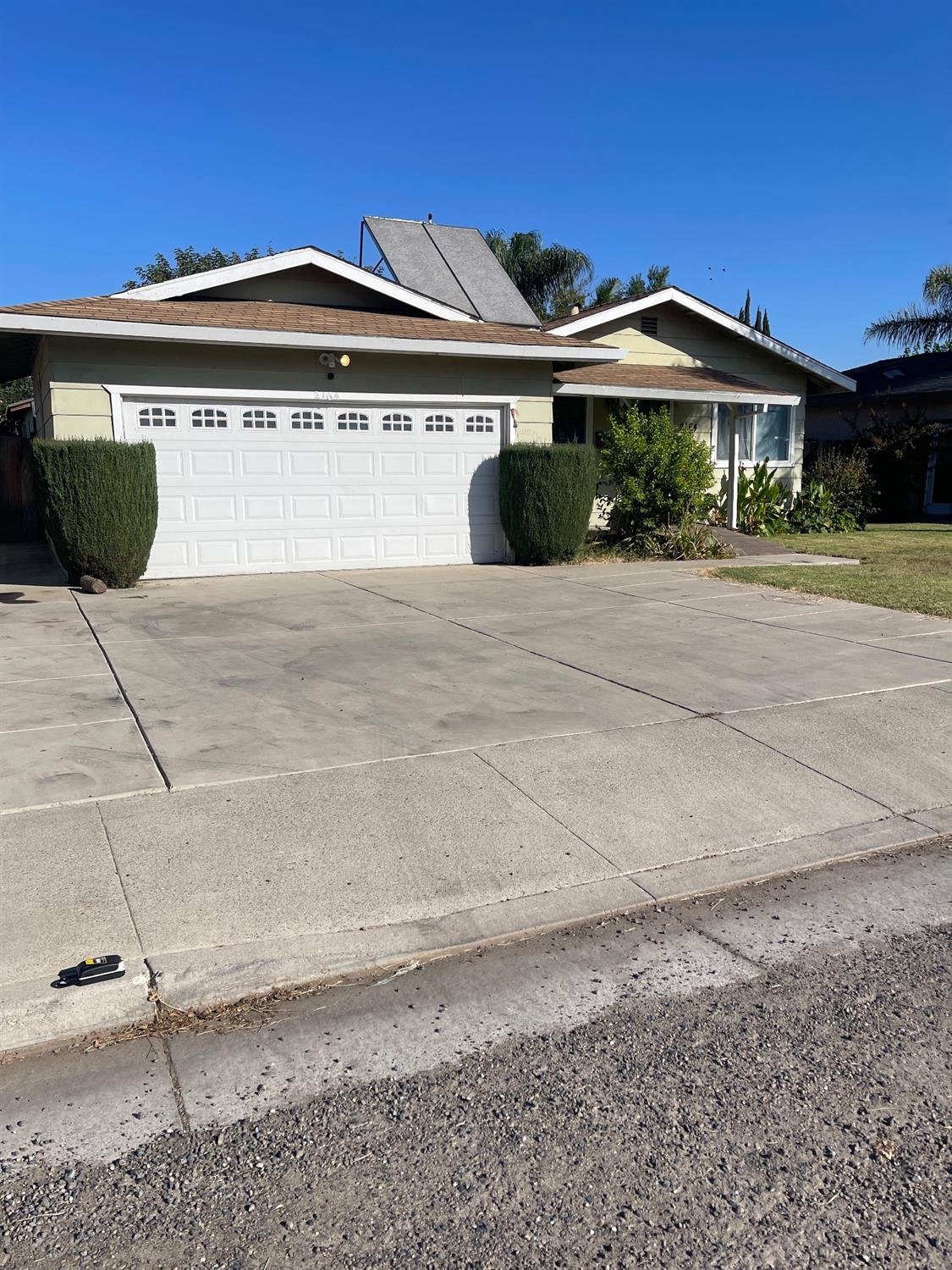 Single-story home with a wide white garage door, broad concrete driveway, and trimmed hedges.