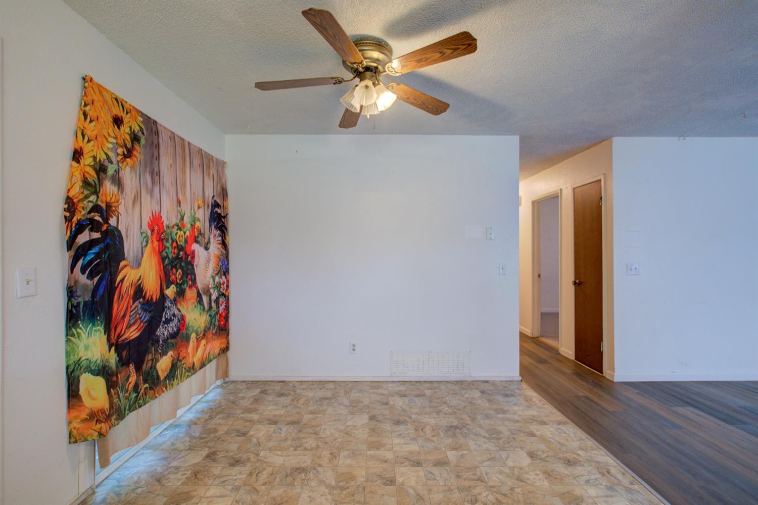 Empty room with beige tile flooring, a ceiling fan, and a colorful rooster mural.