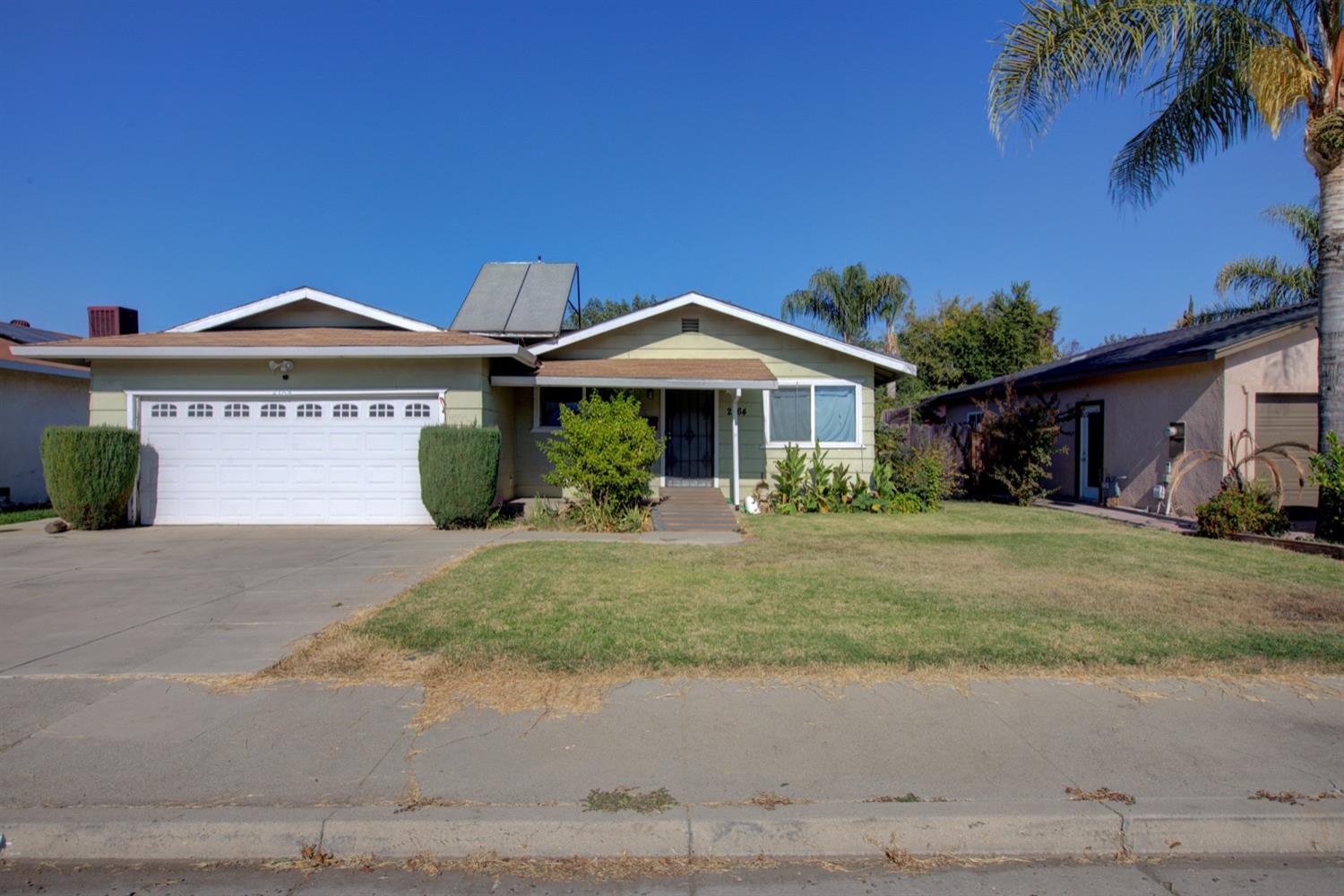 Single-story green house with a double garage, covered porch, driveway, and front lawn.