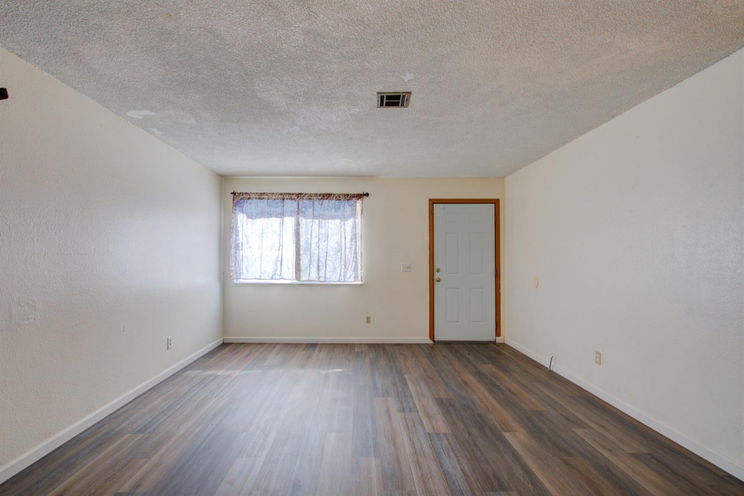 Empty room with plank flooring, a curtained window, and a gray entry door.
