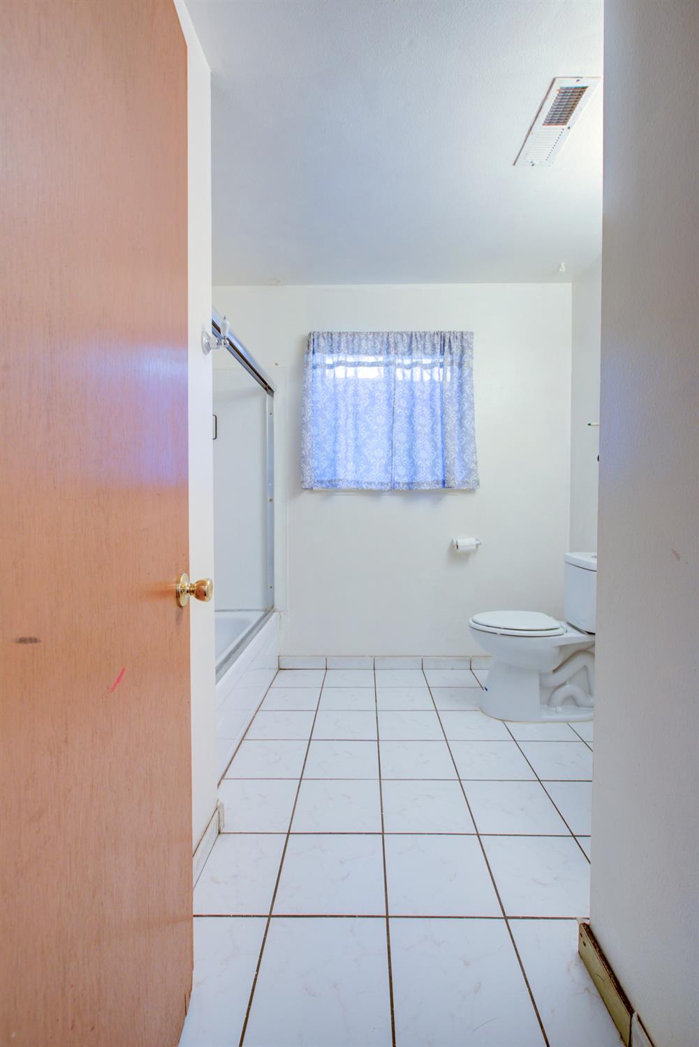 Bathroom with a bathtub, toilet, white tile floor, and curtained window.